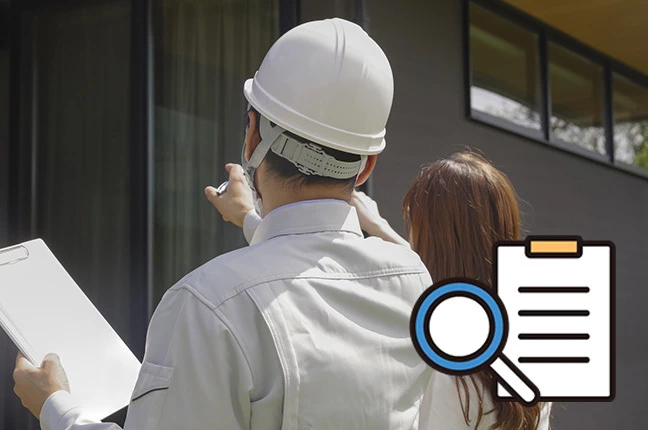 一軒家の前で、ヘルメットを被った専門家が居住者に診断結果を説明している様子